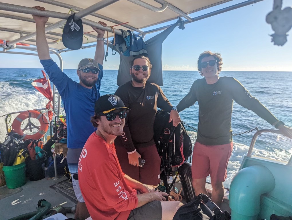 Crew of 4 on a boat smiling for the camera.