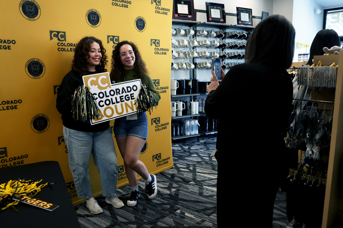 Two students pose in front of a CC backdrop in the bookstore with a CC bound sign and pom poms
