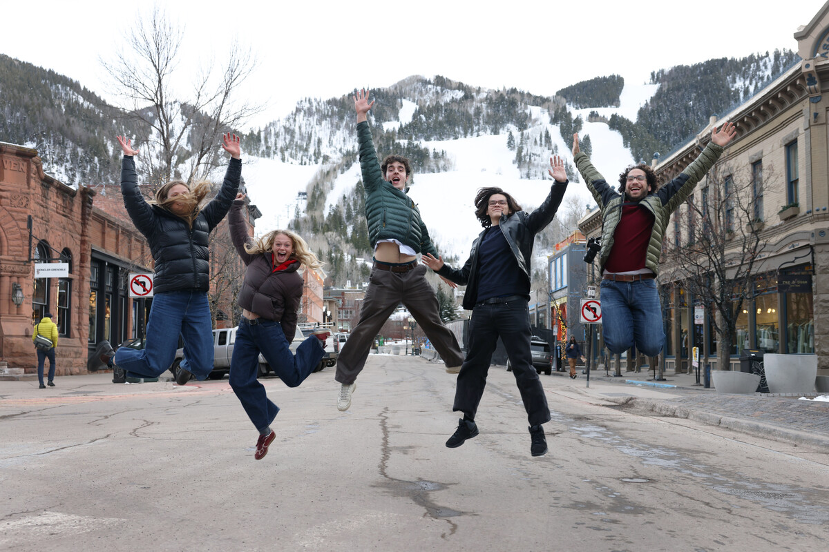 students jumping in a street in Aspen with a snowy mountain backdrop