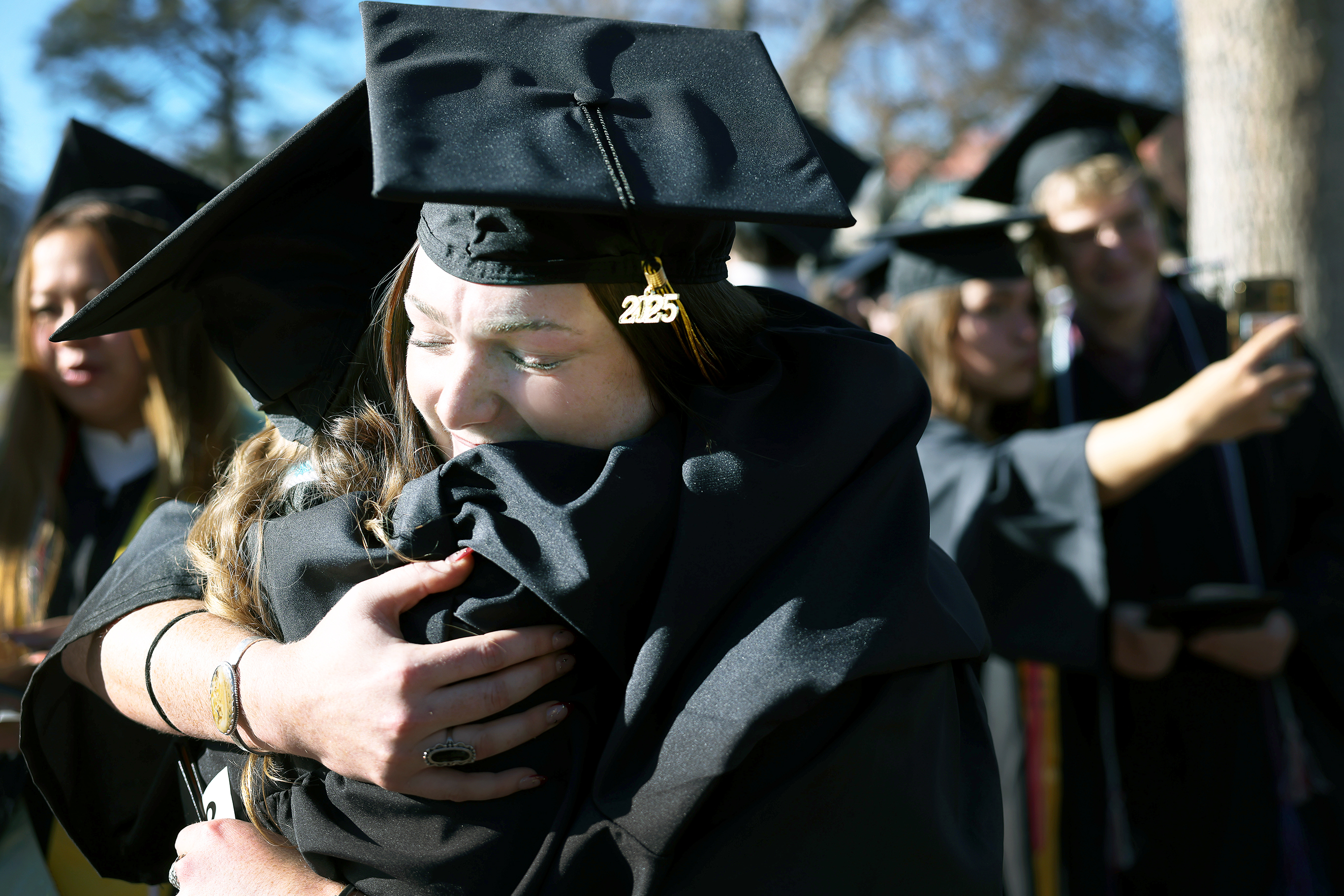 Ryan Maguire '26 shares a hug of congratulations with a good friend while others take selfies with friends following the ceremony of Winter Commencement on December 14, 2025. Photo by Jamie Cotten / Colorado College