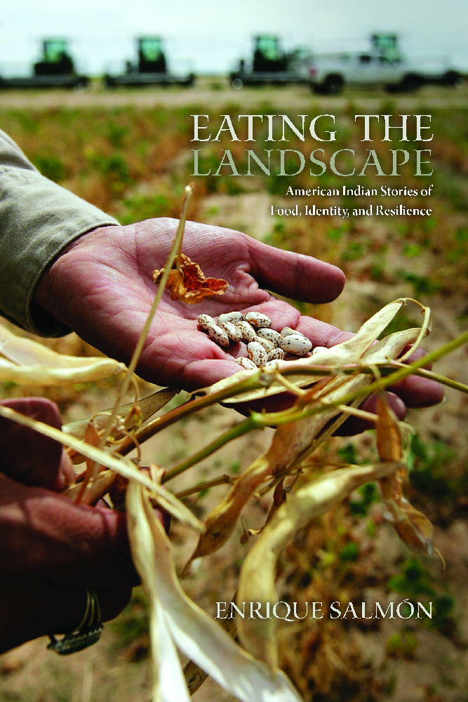 Eating The landscape book cover. Image of a hand holding recently harvested beans with farmland and harvesters in the background.