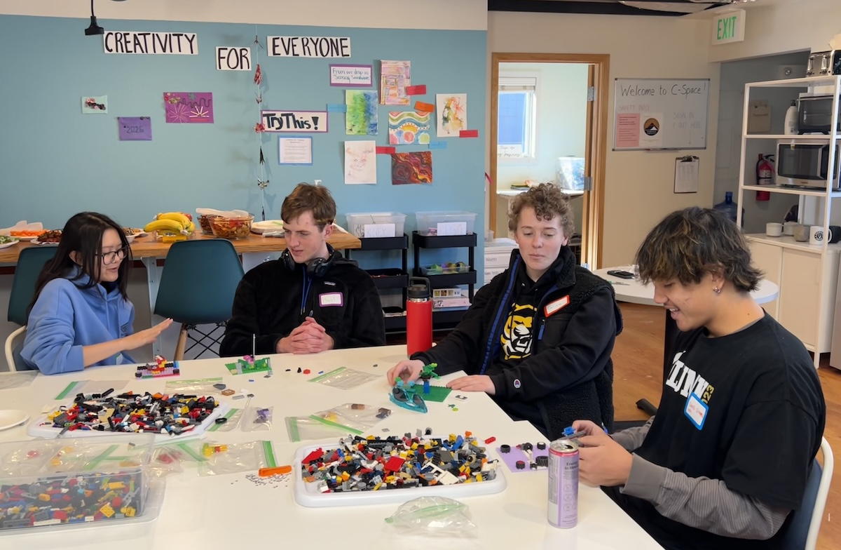Four students sit by a table and play with LEGO